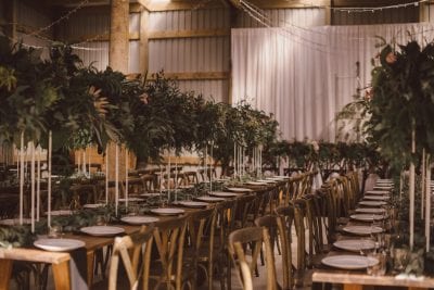 Wooden cross back chairs with tall greenery arrangements on white stands